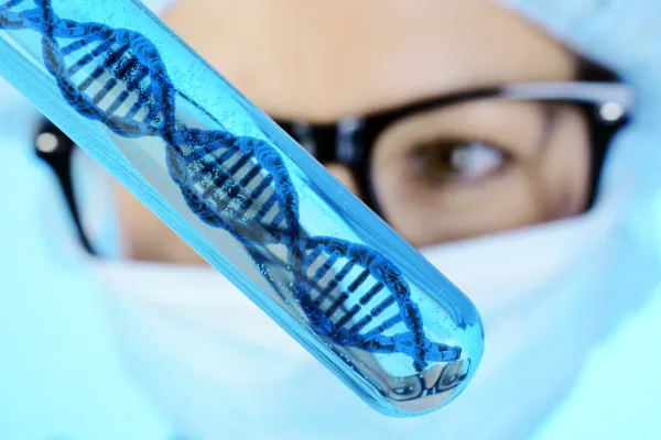 Glasröhrchen mit grafischer DNA-Doppelhelix, im Hintergrund eine Wissenschaftlerin